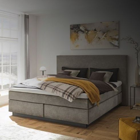 Ein Schlafzimmer mit einem großen, bequemen Boxspringbett in Grau, dekoriert mit einer karierten Decke und Kunst an der Wand.